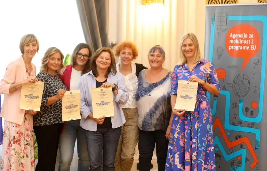 Dobitnice Europske nagrade za inovativno proučavanje poziraju skupa sa svojim priznanjima.  U pozadini se nalazi banner Agencije za mobilnost i programe EU te zastave RH i EU.